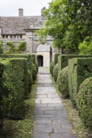 Path of flag stones leading through clipped Yew to arch at entrance to the garden with view to the house. July. Summer