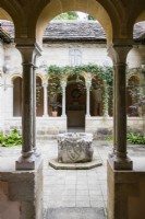 View through arch in the cloisters to a font in the middle of the courtyard with some planting. July. Summer