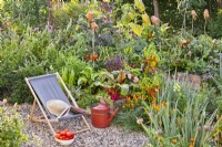 Deckchair on gravel and raised bed with growing crops in kitchen garden.