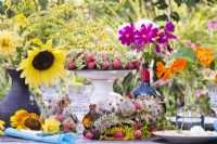 Outdoor dining table setting decorated with yellow, pink and orange themed bouquets in vases including sunflower, solidago, cosmos and nasturtium.