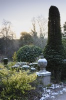 Finial dusted with snow in a formal garden in December, amongst clipped evergreens including yew and box.