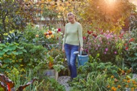 Woman carrying watering can in kitchen garden at sunset.