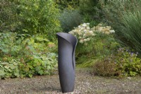 A sculptural pot by Adrian Bates rests in a woodland glade, edged in hardy geraniums and a clump of bullwort.