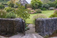 A gate opens into the stream garden, and the bridge and path passes between a miscanthus and dogwood to the lawn, at its centre a kidney-shaped bed of perennials and grasses.