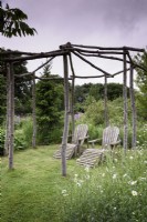 A pair of wooden recliners below a rustic arbour in May