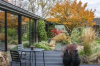 View from the house of a contemporary courtyard  (20m x 18m)  with gravel paths, reclaimed water tanks filled with plants or water, and raised beds of drought tolerant plants beneath the canopy of a Japanese maple, green until autumn turns the leaves gold.
