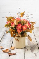 Arrangement of orange roses and Autumn Fagus - Beech leaves in pottery vase on rustic wooden table