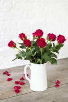 Red roses arranged in white china jug against rustic background