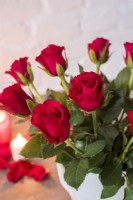 Closeup of red roses in white jug with lighted candles in background
