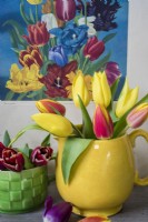 Yellow and red tulips arranged in yellow jug with vintage poster in background