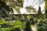 Country garden in September featuring clipped evergreens and flowering plants framed by a hedge.