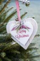 Frosty wooden heart with 'Merry Christmas'  hanging from tree in the garden