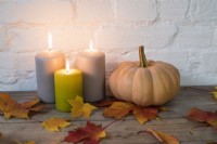 Trio of lighted pillar candles and 'Autumn Crown' pumpkin with autumn leaves on wooden background