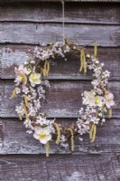 Rustic wreath decorated with Prunus spinosa blossom, Helleborus orientalis flowers and Salix catkins hanging on fence