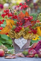 Bunch of guelder rose twigs with red berries and autumn foliage in terracotta pot.