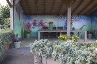 Painted flowers on wall of veranda and green plastic containers on wooden painted table.