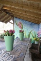 Painted flowers on wall of veranda and green plastic containers with pink Hyacinth and white pink tulips on wooden painted table.