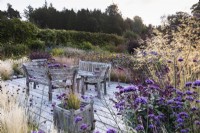 Decking with wooden planters and furniture surrounded by planting including Verbena bonariensis and grasses at Whitburgh House Walled Garden in September.