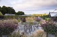Decked area with wooden seating surrounded by ornamental grasses and late season flowering perennials including Verbena bonariensis and containers of salvias.