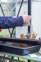 Woman using a compost sieve to evenly spread compost over the seeds