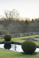 Clipped yew spheres framing the formal lily pond on the Jewson Terrace at Cotswold Farm Gardens in February