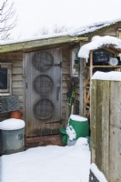Small leanto garden shed and well-organised covered storage area with garden sieves, tools and containers. Snow. December.