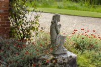 Young girl statue with rock roses Helianthemum and gravel pathway and grass beyond.