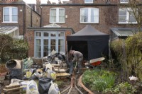 Construction materials and a worker at the start of the makeover of a small London garden.