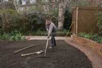 A worker raking the ground in preparation for laying new turf during the makeover of a London garden.