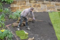 A garden worker raking soil in preparation for laying turf during a garden makeover.