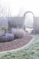 Archway in garden with grass and shrubs covered in frost