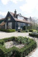 View of farm house nursery de Boschhoeve with topiary hedges in front garden. Black painted wood.