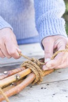 Woman tying the birch sticks together with rope to create a stand for the dish