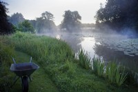 Morning mist on the river Nar. Wheelbarrow on lawn edge.
