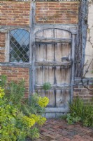 View of an old wooden door suurounded by foliage plants in a country garden in Spring - April