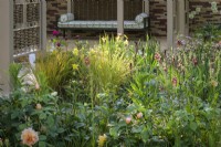 Herbaceous beds planted with  lupins,  white alliums, geums, astrantias, pimpinella, verbascums and ornamental grasses. in front of pavillion made of willow screens  - Stitchers Sanctuary Garden
