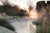 The sun illuminates mist rising from the moat at The Bishop's Palace in Wells on a January morning.