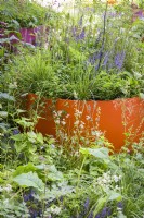 Large orange planter filled with plants and surrounded by perennials -The St Mungo's Putting Down Roots Garden 