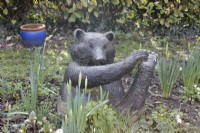 A bronze resin bear sculpture sits in a winter flower bed. Sculpture made by Suzi Marsh. February. 