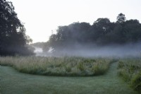 Early morning mist on the river Nar with area of mown lawn and wild grass.
