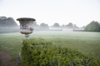 Old urn by Yew hedge. Distant mist in the early morning.