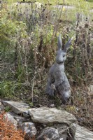 Alert hare, bronze cast sculpture by Suzi Marsh, amongst dead border growth. February. 