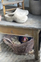 Chicken in basket breeding under table with wooden clogs.