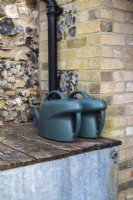 Plastic watering cans resting on top of metal water butt