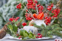 Winter arrangement with frozen cake, spruce branches and bouquet of Chinese lanterns and guelder rose twigs with berries.