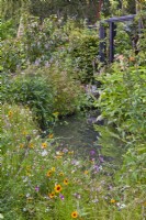 Mixed natural planting around pond and pergola in background.