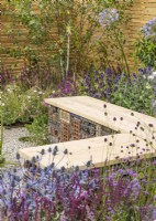 L-shaped wooden bench incorporating 'bug hotel' underneath, surrounded by drought resistant plants in gravel, summer July