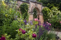 Summer in the Kitchen Garden at Morton Hall Gardens with a mixed border against the brick wall with an arch behind. Rosa 'Falstaff' and 'Boscobel'.
