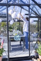 Woman hanging paper pom poms in greenhouse