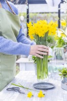 Woman placing glass vase of daffodils on table